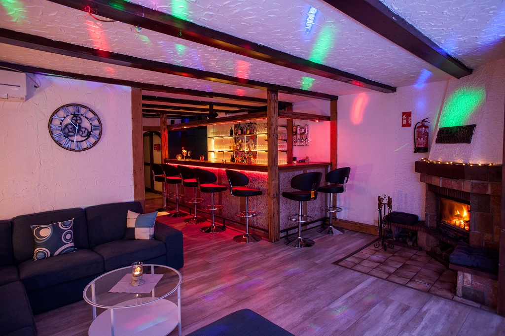 Bar mit Hockern, dunklen Sofas und einem brennenden Kamin.
